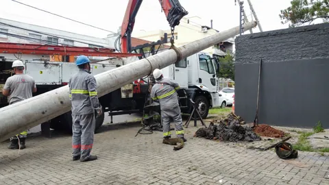 Equipe acompanhando a movimentação de poste de concreto com guindaste
