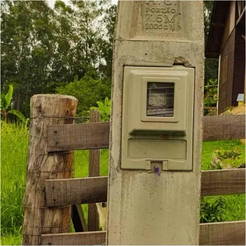 Caixa de medição em poste de concreto junto a uma cerca de madeira