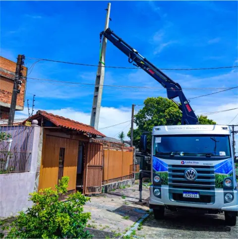 Caminhão guindaste içando poste de concreto em rua residencial
