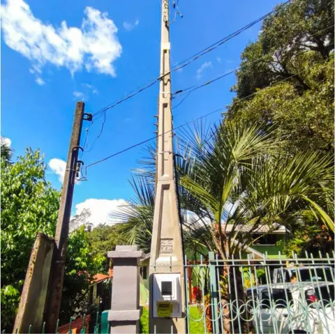 Poste de entrada de energia junto a um portão e vegetação