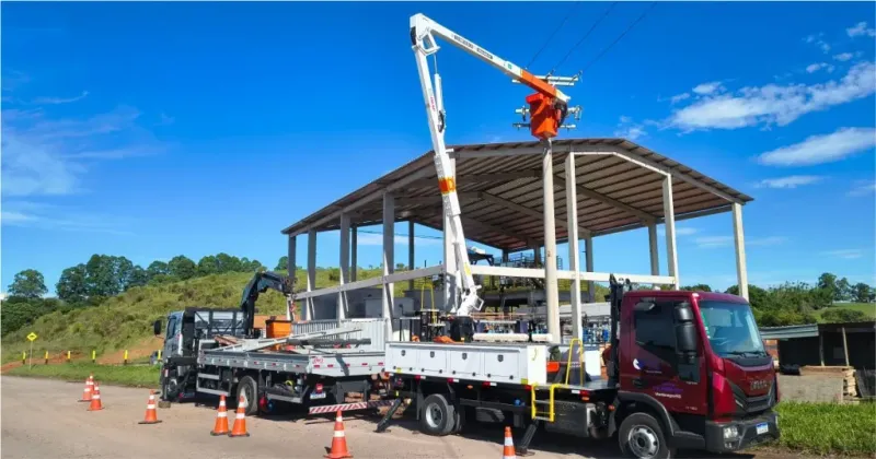 Caminhão com plataforma aérea elevada próximo a uma estrutura industrial