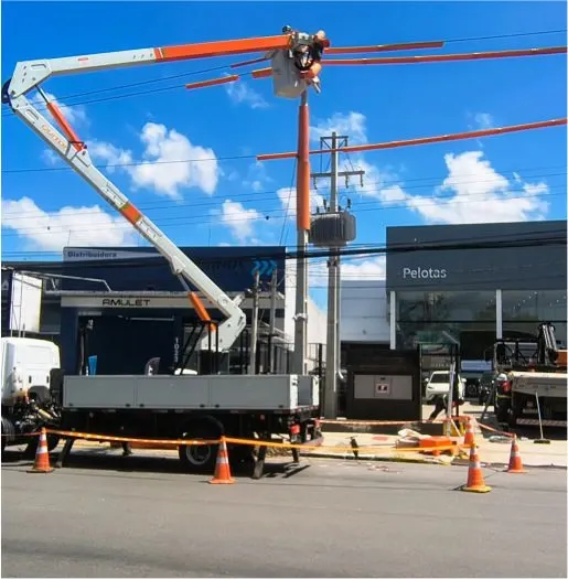 Caminhão com cesto aéreo junto a poste em frente a uma edificação comercial