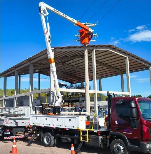 Caminhões e plataforma aérea próximos a uma estrutura industrial