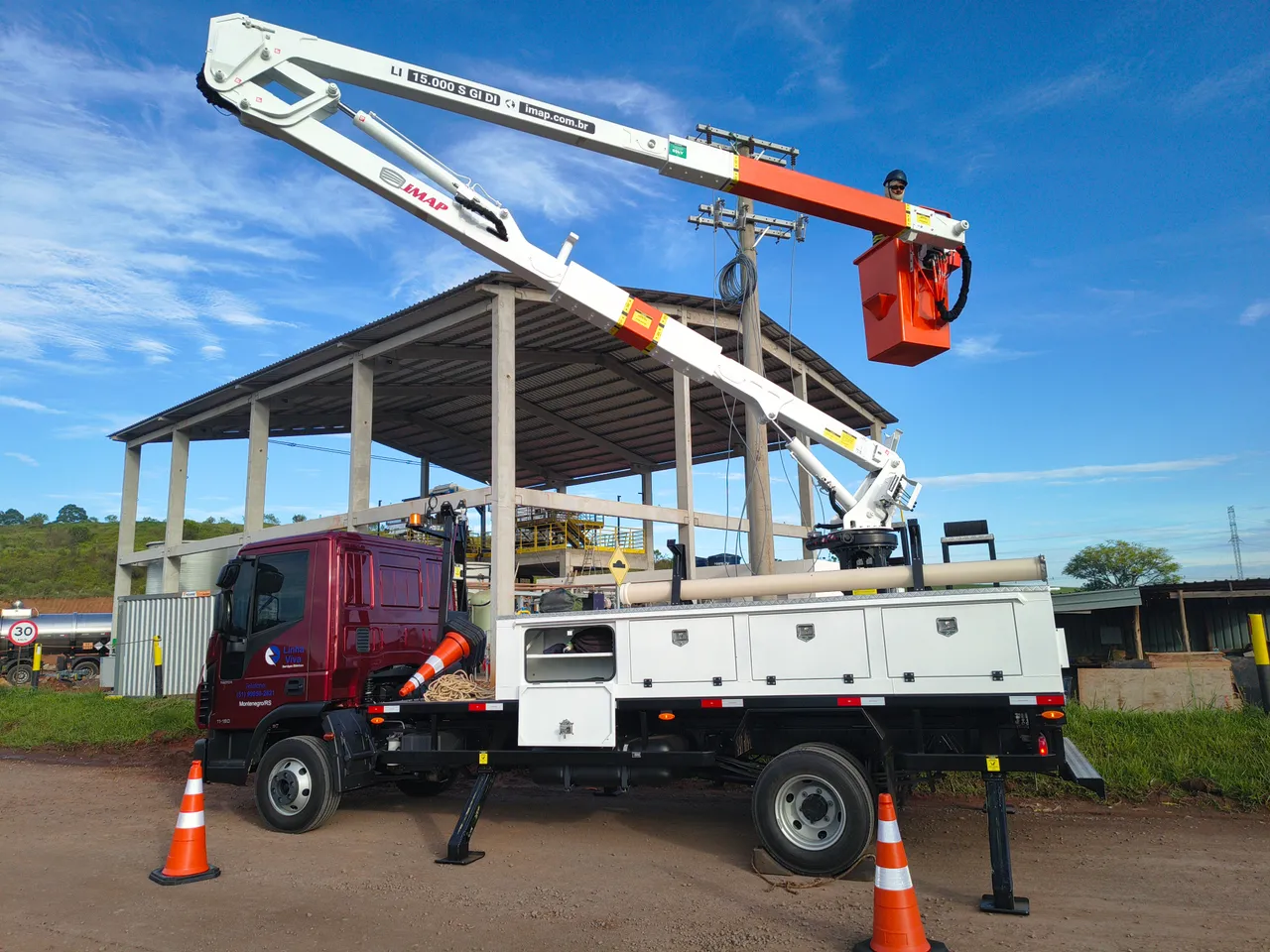 Caminhão com cesto aéreo elevado ao lado de estrutura metálica