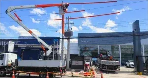 Caminhão e cesto aéreo posicionados junto a um poste em área comercial