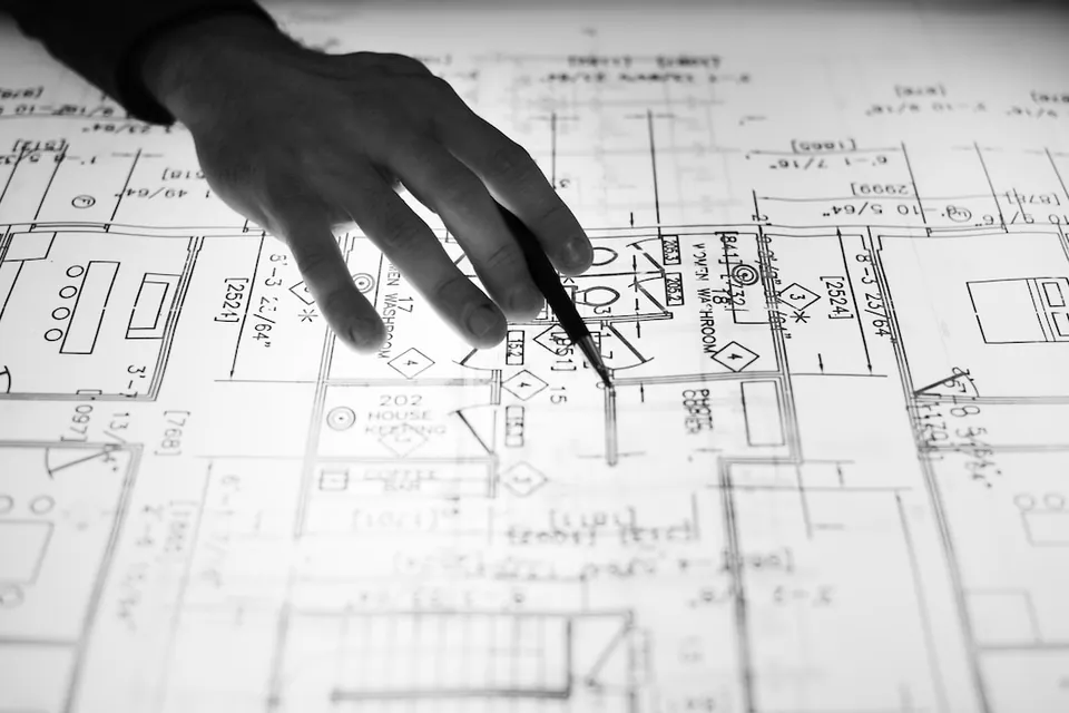 Detalhe de planta técnica com cotas e símbolos, apontada por um lápis