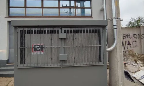 Cabine de alvenaria com grade metálica junto ao poste e à fachada do edifício